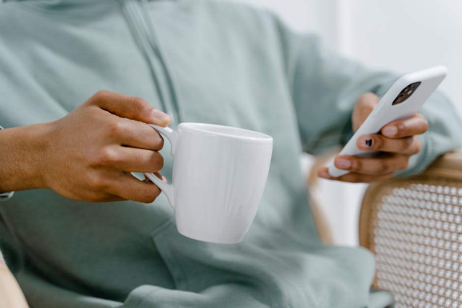 A person holding a phone with a calm, minimal planning app visible on the screen, morning coffee nearby