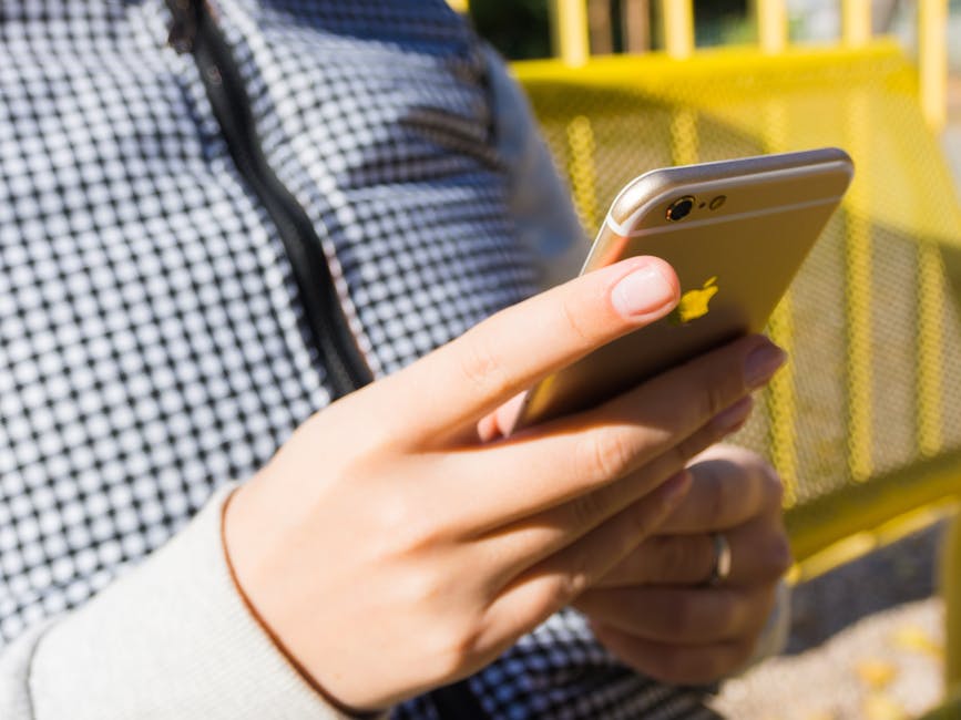A parent looking at an iPhone calendar app while standing outside a school building in afternoon light