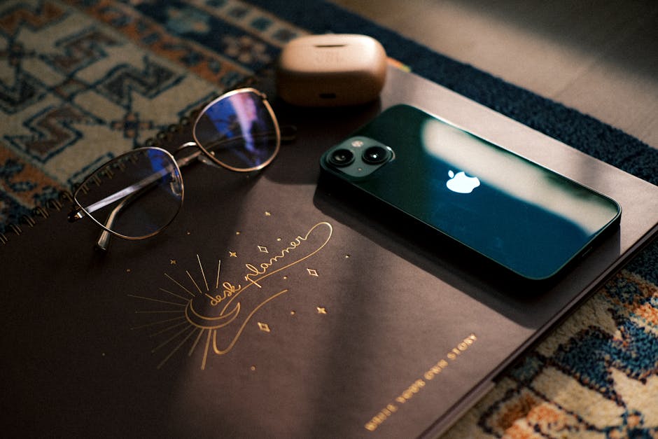 A clean wooden desk with an iPhone, small notebook, and cup of coffee in soft morning light