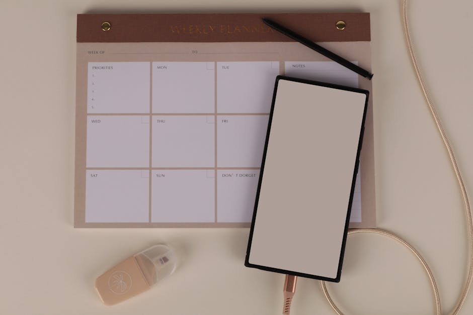 A smartphone showing a clean calendar app on a wooden desk with a small succulent and a notebook nearby