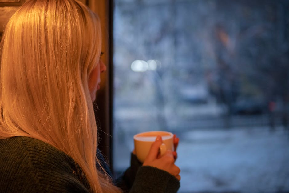 A person sitting by a bright window with a coffee mug, looking out calmly