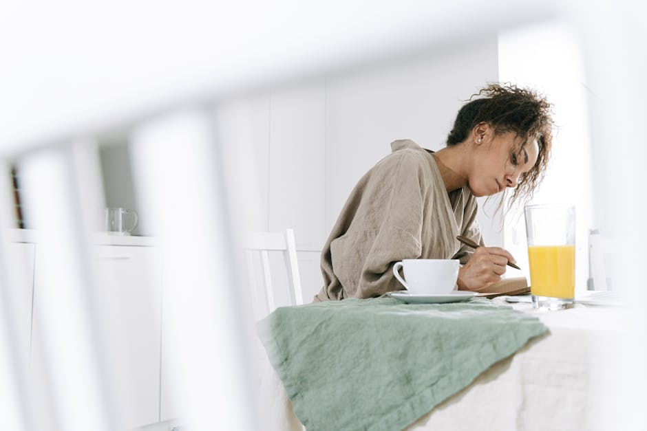 A ceramic mug of coffee sitting on a wooden table next to an open notebook in soft morning light