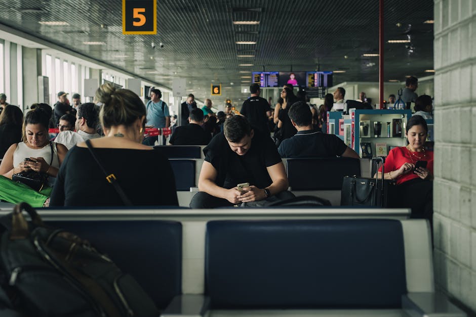 A person sitting at an airport gate calmly looking at their phone with a carry-on bag beside them