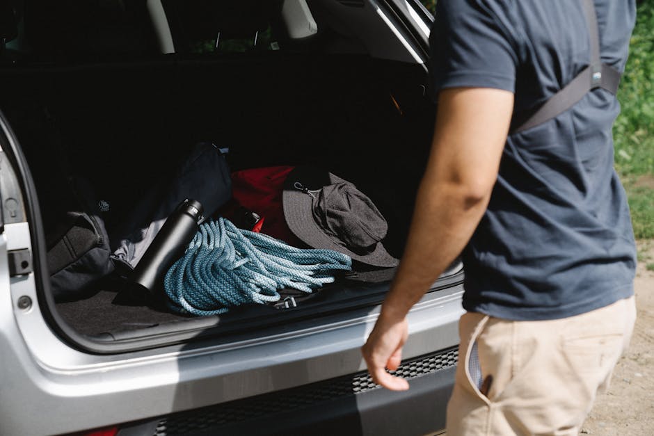 An open car trunk packed with bags, a cooler, and road trip snacks in afternoon sunlight