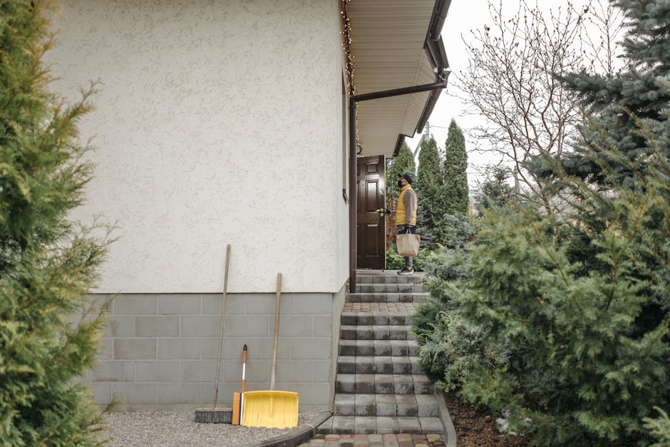 A person pulling on a jacket and picking up a bag near a sunlit front door, ready to leave