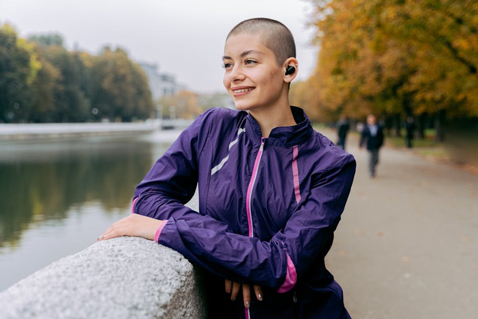 A person walking along a tree-lined path in warm autumn light, wearing white earbuds