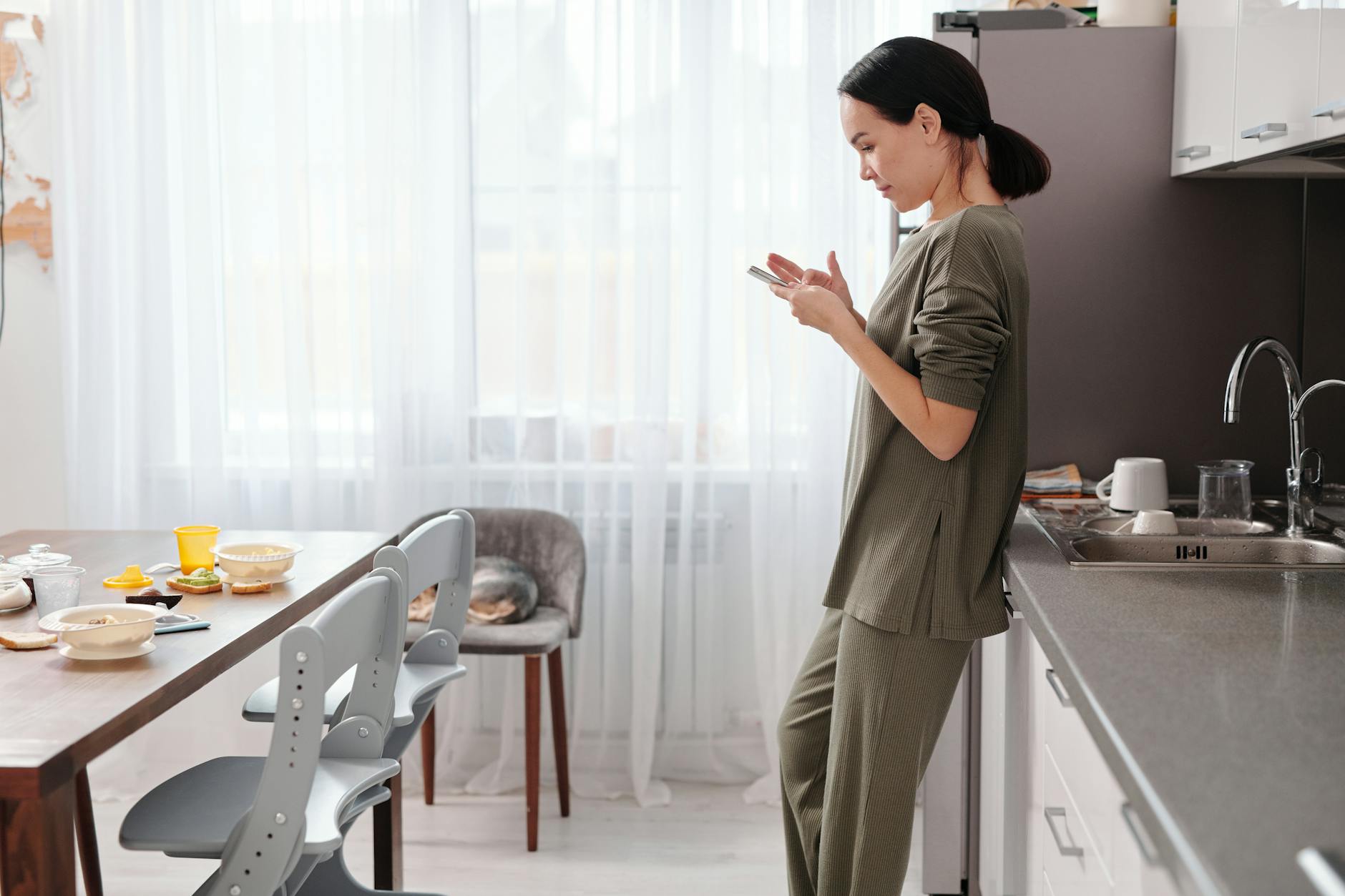A woman in a cozy kitchen nook, speaking naturally to her phone while morning light streams in