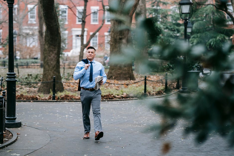 A person walking down a tree-lined sidewalk with purpose, looking ahead with a slight smile