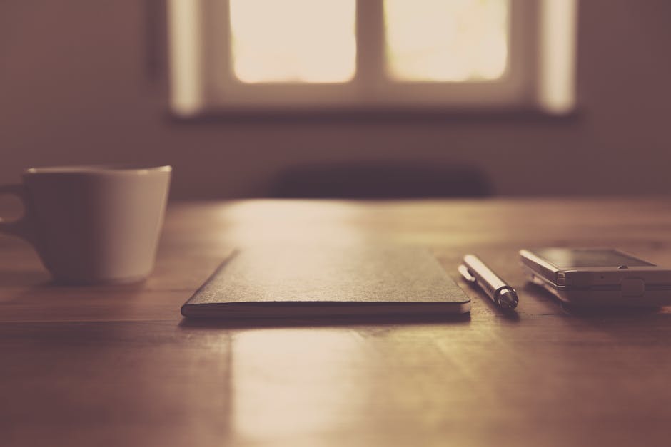 A person's hands around a warm mug on a clean wooden desk, soft morning light coming through a window
