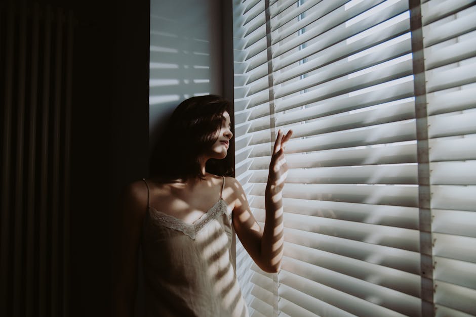 A person sitting by a window in soft morning light, holding a warm drink and looking thoughtfully outside